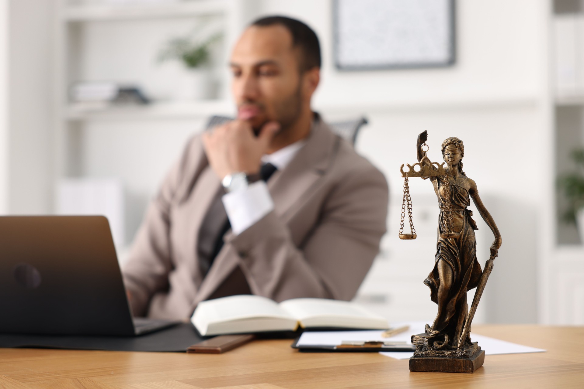 Lawyer working with laptop at table in office, focus on statue of Lady Justice